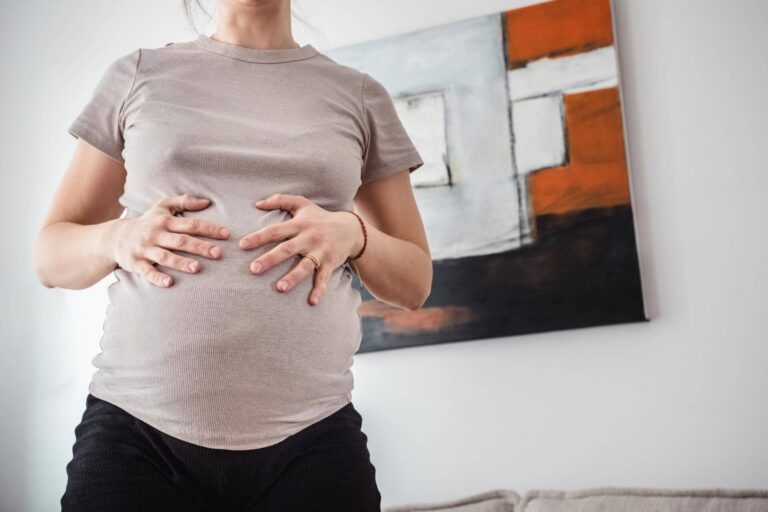 Eine schwangere Frau hält im geschützten Zuhause liebevoll ihren Babybauch. Ein ungestellter, intimer Moment in den letzten Tagen vor der Geburt, fotografiert von Doula und Geburtsfotografin Kasia Warpas in München.