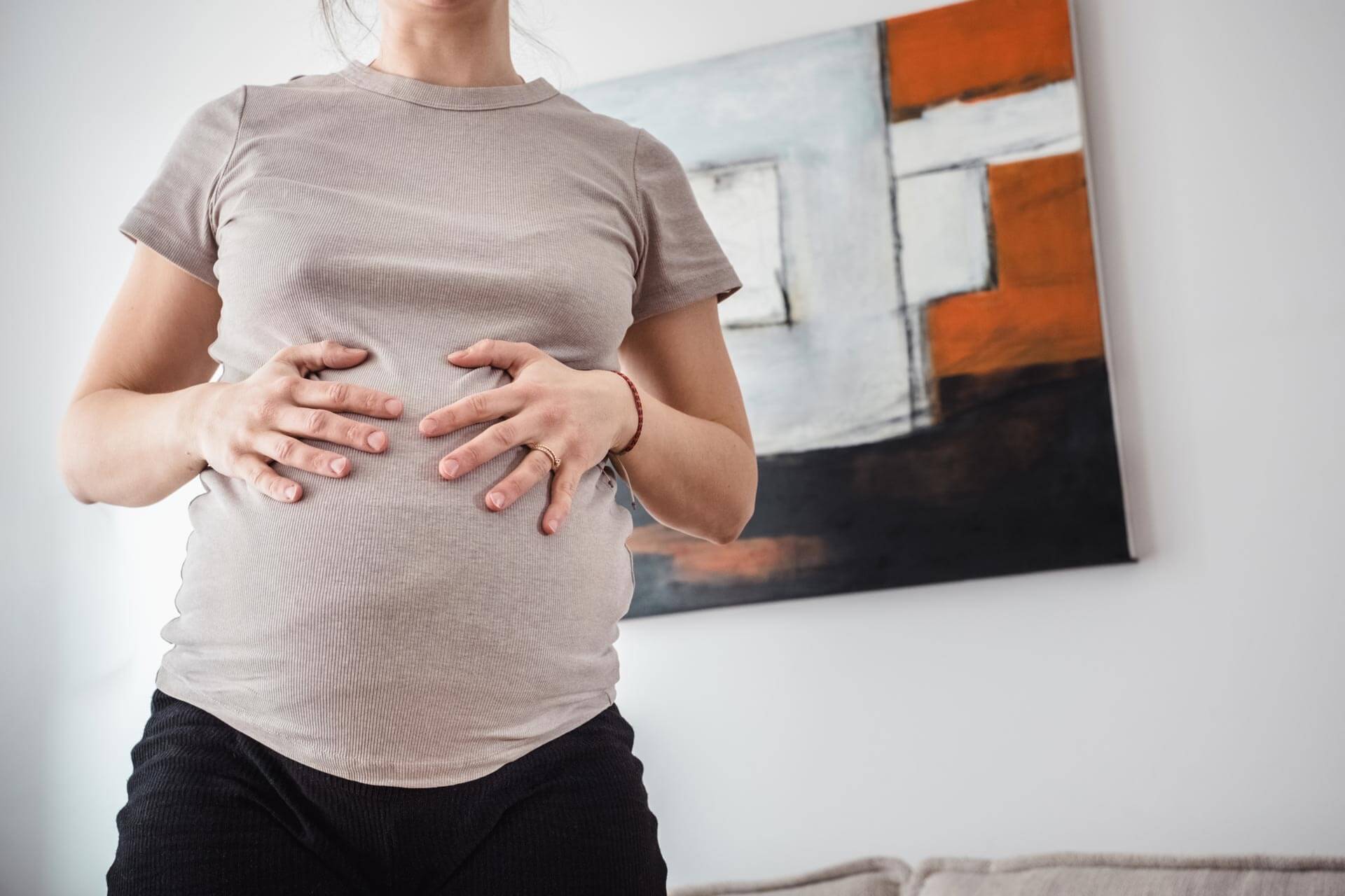 Eine schwangere Frau hält im geschützten Zuhause liebevoll ihren Babybauch. Ein ungestellter, intimer Moment in den letzten Tagen vor der Geburt, fotografiert von Doula und Geburtsfotografin Kasia Warpas in München.